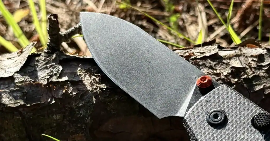 Macro photo of Vosteed Raccoon black stonewashed blade laying on a tree branch on the ground