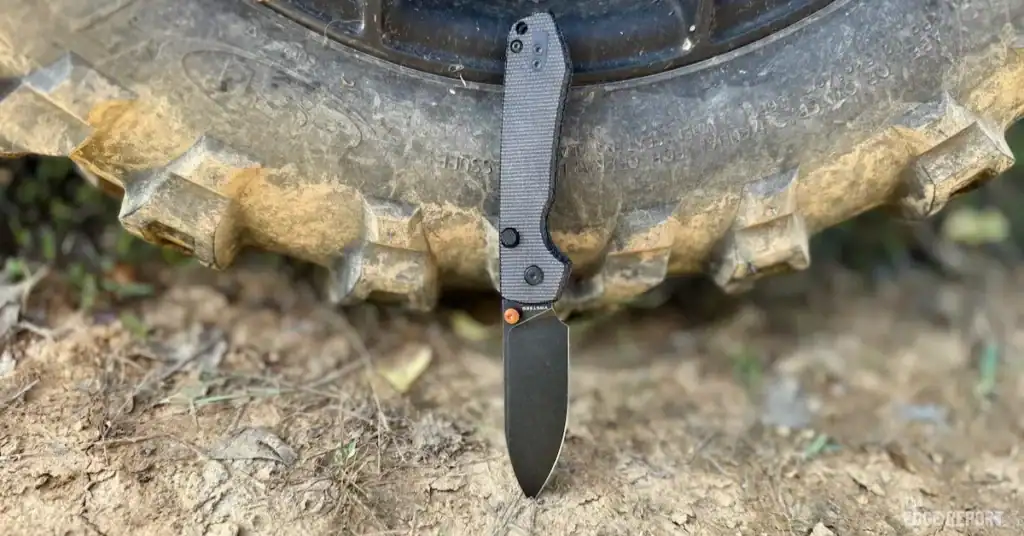 Vosteed Raccoon leaned up against a Side by Side tire on red clay dirt.