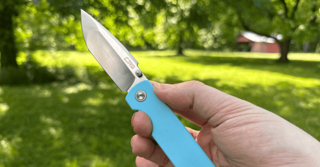 CJRB Nova in Baby Blue G10 scales, open in hand showing a side profile against a beautiful country scene